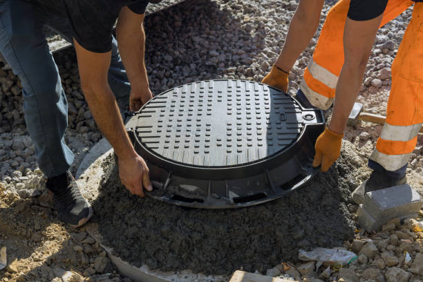 A worker installs a sewer manhole on a septic tank made of concrete rings with construction of sewerage